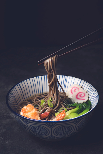 Japanese Soba noodle soup with shrimp tempura or Nabeyaki udon on the dark rustic background. Tagliatelle made from buckwheat flour, winter food