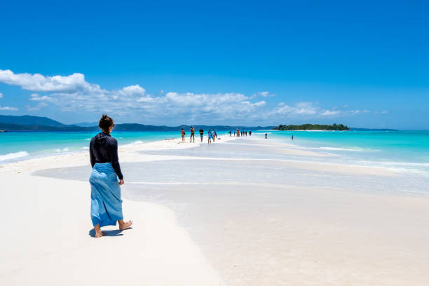 Female tourist wears sun protection all over her body and walks along the paradisiacal white sandy beach with other tourists and the turquoise blue, clear water. Nosy Be, Nosy Iranja, Madagascar, Africa. Description: Female tourist wears sun protection all over her body and walks along the paradisiacal white sandy beach with other tourists and the turquoise blue, clear water. Nosy Be, Nosy Iranja, Madagascar, Africa. madagascar beach photos stock pictures, royalty-free photos & images