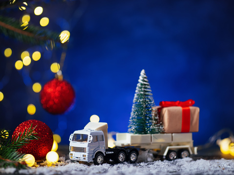 A toy truck is transporting a Christmas tree, blue background.