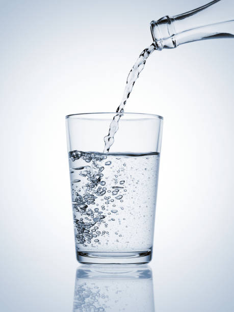 istock Water pouring from a bottle in a glass with bubbles on blue background 1817320079