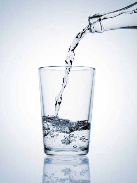 istock Water pouring from a bottle in a glass with bubbles on blue background 1817320080