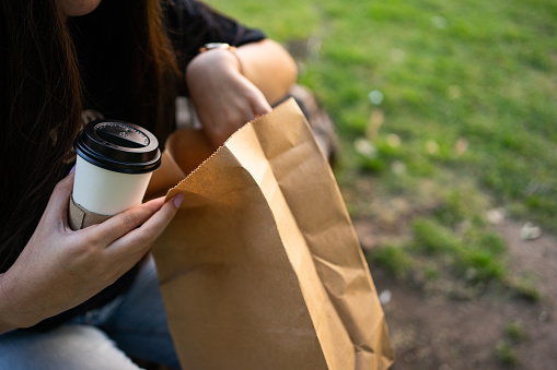 A girl opening a bag of croissants while having coffee in the park. With Copyspace