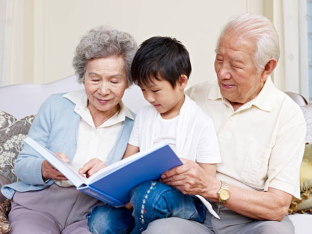 Grandparents reading to their grandson grandparents and grandson reading a book together. china chinese ethnicity smiling grandparent stock pictures, royalty-free photos & images