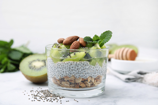 Delicious dessert with kiwi, chia seeds and almonds on white table, closeup