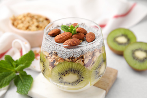 Delicious dessert with kiwi, chia seeds and almonds on light table, closeup