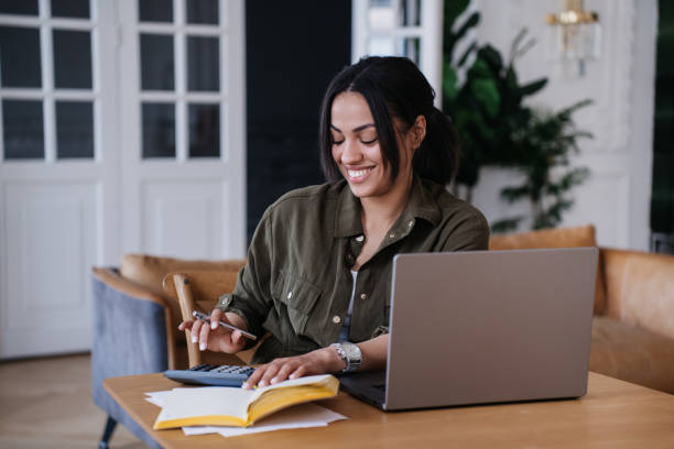 istock Cheerful accountant using calculator sitting at desk with laptop, smiles broadly, enjoying work at home, distant job, remote working people. Self isolation during virus pandemic. Businesswoman. 1817361922