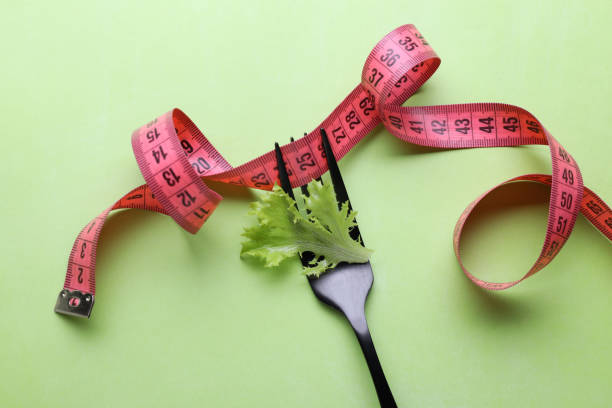 薄緑色の背景に巻尺とレタスの葉とフォーク、平らな置き場。ダイエットのコンセプト - instrument of measurement vegetable measuring exercising ストックフォトと画像