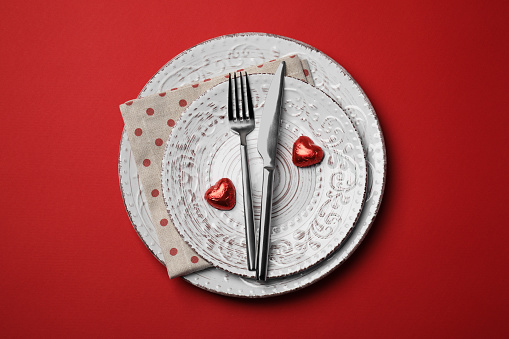 Beautiful place setting with dishware and sweets for romantic dinner on red table, top view