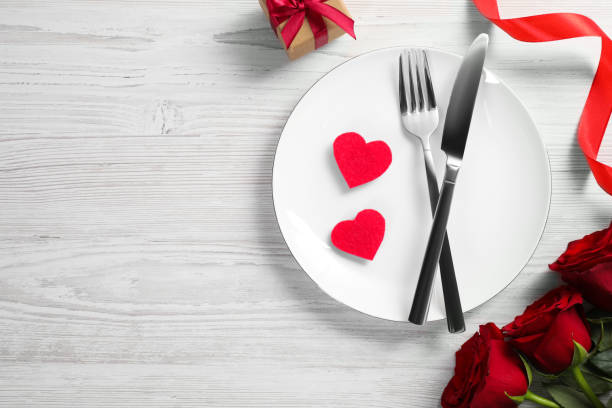 istock Beautiful place setting with dishware, gift and bouquet for romantic dinner on white wooden table, flat lay. Space for text 1817383779