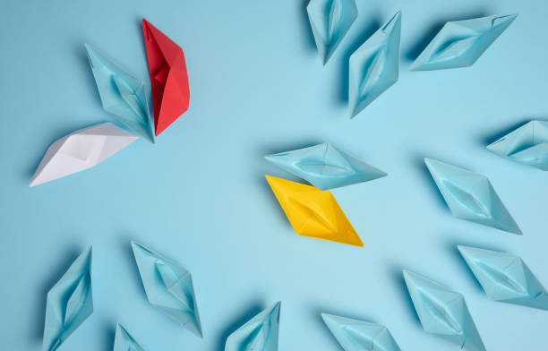 istock A group of paper ships against another aggressive group on a blue background. Association concept, top view 1817390551