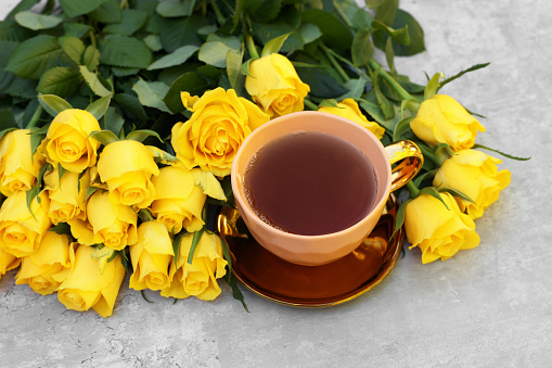 Cup of tea and beautiful yellow roses on light table, above view