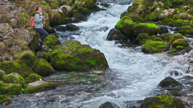 AERIAL Drone Shot of Woman Relaxing Near Stream Flowing Through Stones Covered With Moss in Forest