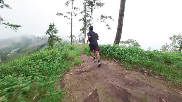 Athlete sport: young Asian man running trail through the forest on a mountain for fitness, adventure, and outdoor livestyle from an FPV. aerial point of view with a drone.