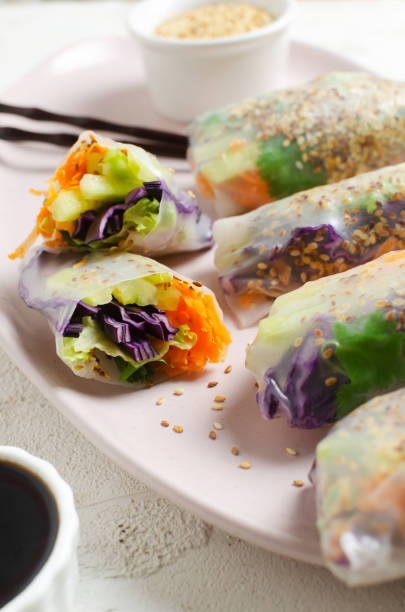Vegetarian vietnamese spring rolls with carrot, cucumber, red cabbage, cilantro, sesame and rice noodle on a pink plate. veggie dish. Vegan food. Vertical orientation. Selective focus stock photo