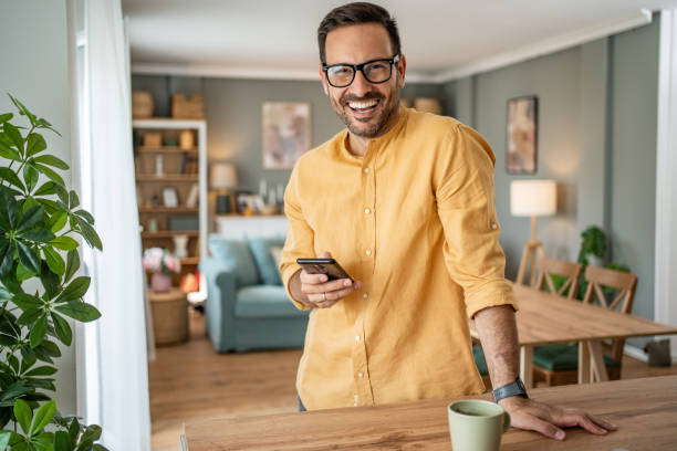 Portrait of cheerful man using smartphone at home Portrait of cheerful man using smartphone at home, daily routine man 30 years old stock pictures, royalty-free photos & images