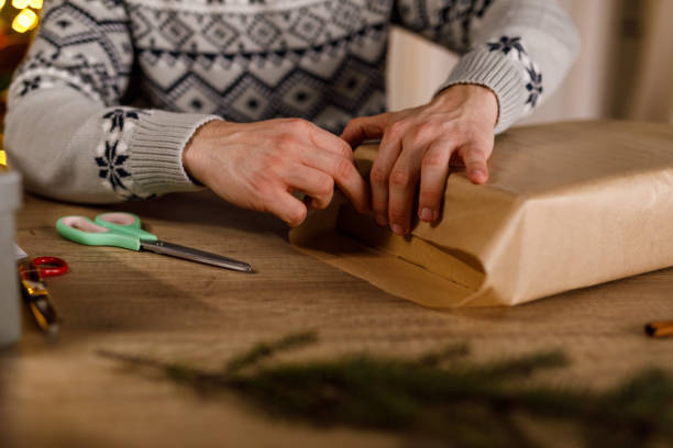 istock Young man folding edges of a rustic brown paper that he is using to wrap a Christmas gift box 1817456894