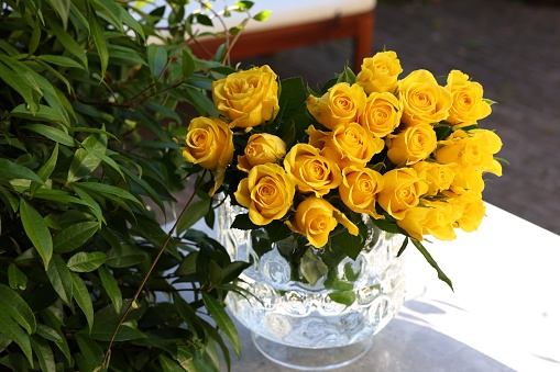 Beautiful bouquet of yellow roses in glass vase on white table outdoors