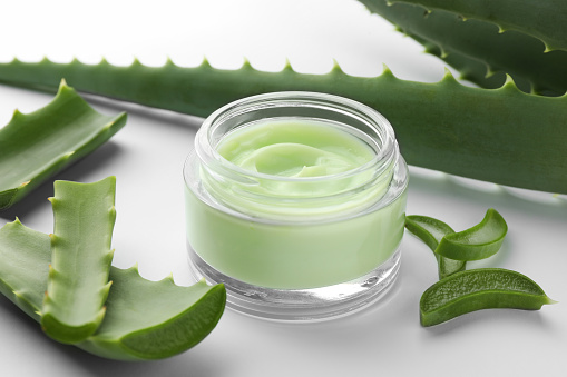 Jar of natural cream and aloe leaves on white background, closeup