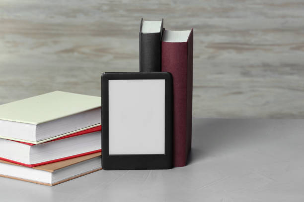 istock Portable e-book reader and many hardcover books on white textured table, space for text 1817498010