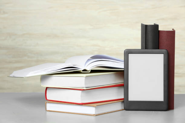 istock Portable e-book reader and many hardcover books on white textured table 1817498535