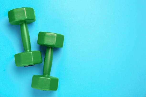 istock Green dumbbells on light blue background, flat lay. Space for text 1817511472