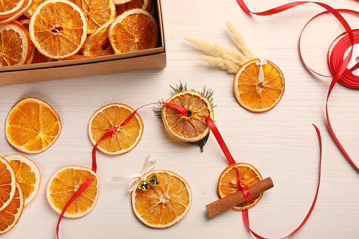 Beautiful garland with dry oranges, cinnamon, ribbon and sleigh bells on white wooden table, flat lay