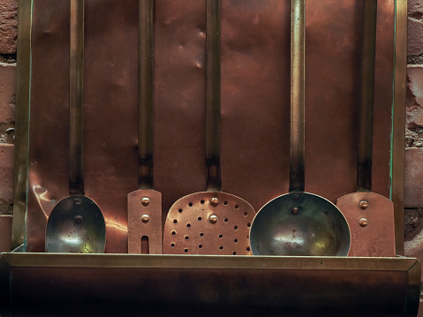 Vintage rustic copper kitchen utensils hanging on a shelf on a brick wall. Selective focus.