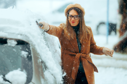 Person using a snow broom to uncover her vehicle from a trip