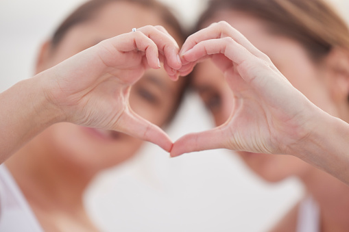 Heart hands, couple of friends and women outdoor with blurred background showing teamwork. Love, care and support hearts emoji hand sign of lgbt pride and solidarity together for valentines day