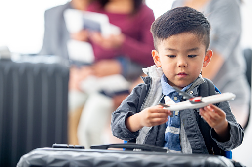 A little boy of Asian decent, plays with a toy airplane, as he waits at the airport with his family.