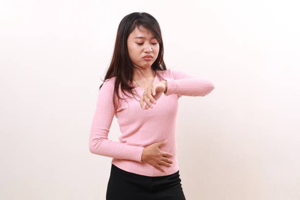 istock Young asian girl standing feeling hungry while checking time on her wrist watch. Isolated on white background 1817710091