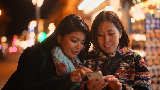 Two female tourist friends are using a mobile smart phone to search places in the city during their travel.