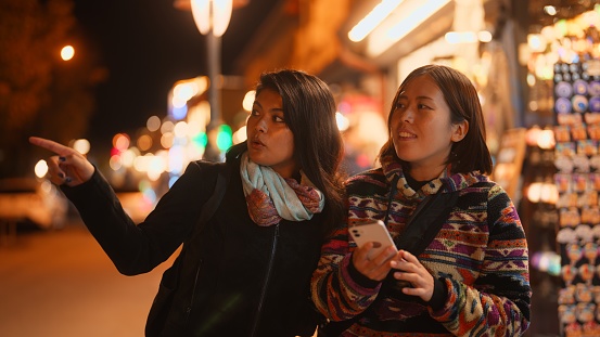 Two female tourist friends are using a mobile smart phone to search places in the city during their travel.