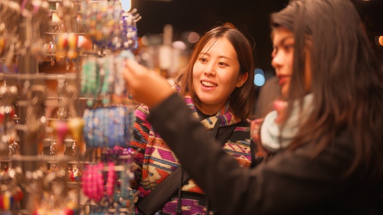 Two female tourist friends are looking for souvenirs in retail shop.