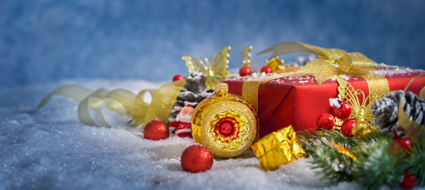 Christmas composition. Christmas tree branches, red gift box with balls, cones and golden decor In the snow on the old wooden table close -up