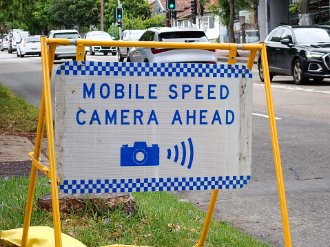 A warning sign is placed on Sydney Road, Fairlight on the northern beaches of Sydney, about 200 meters before the mobile speed camera car parked on the left. Yellow coloured sandbags hold the frame in place.  This image was taken on an overcast afternoon on 4 November 2023.