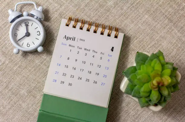 Photo of Desk calendar for April 2024 and a clock on the table.