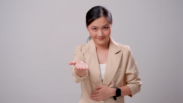 Asian woman smiling confident stretching out open hand welcoming and looking at camera, isolated over white background.