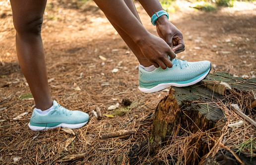 Close-up shot of a young female runner tying her shoelaces before going for a run on forest trail