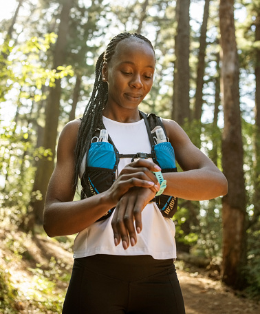 African woman runner checking results on smart watch after training in forest