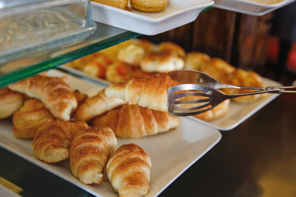 Close-up shot of unrecognizable person picking up a croissant with tongs at bakery store