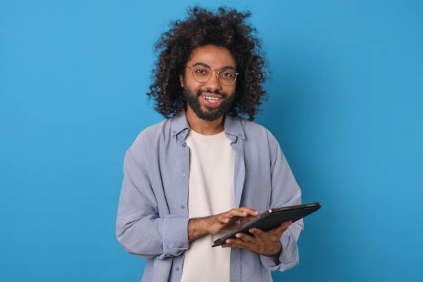 istock Young cheerful Arabian man with beard holds electronic tablet stands in studio 1817938108