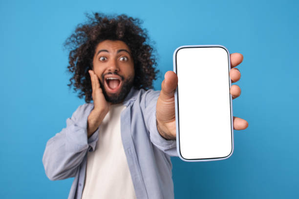 istock Young overjoyed Arabian man with phone opens mouth in surprise stands in studio 1817939694