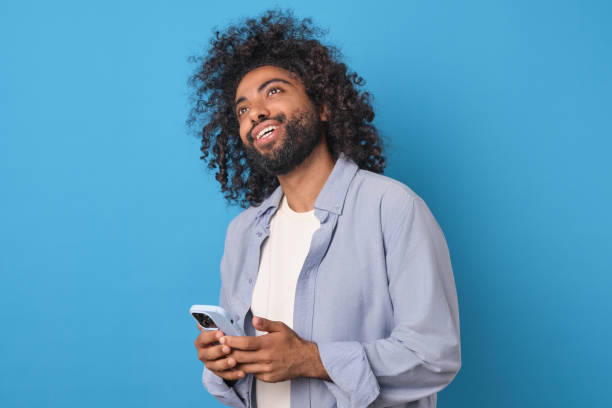 istock Young positive ethnic Arabian man holding mobile phone and smiling looking up 1817941321