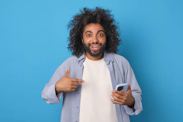 istock Young admiring ethnic Arabian man points finger at smartphone stands in studio 1817942866