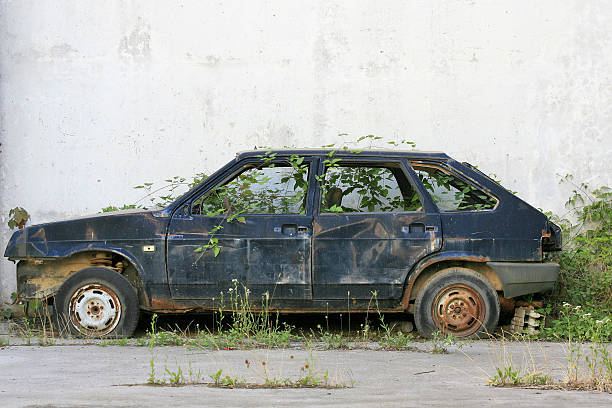 discarded old car discarded old car in overgrown grass next to the wall beat up car stock pictures, royalty-free photos & images