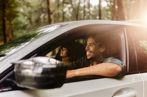 Happy black man driving a car while going on a road trip with his girlfriend.