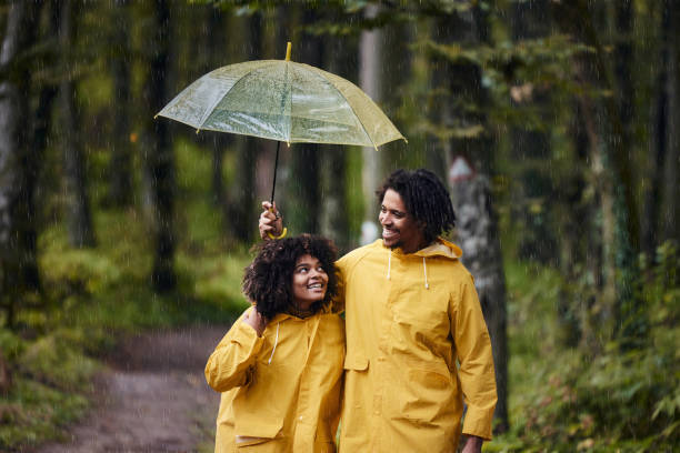 coppia nera felice che cammina in un giorno di pioggia nei boschi. - candid women african descent umbrella foto e immagini stock