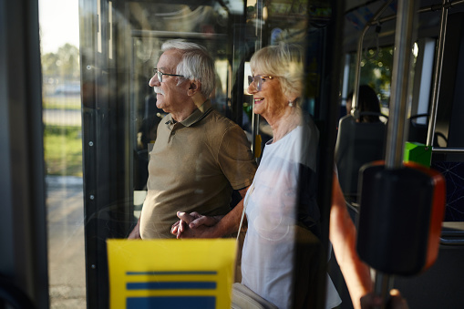 Happy mature woman holding hands with her husband while leaving the bus. The view is through glass.