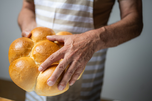 Senior male baker breaking fresh bread buns with hands close up